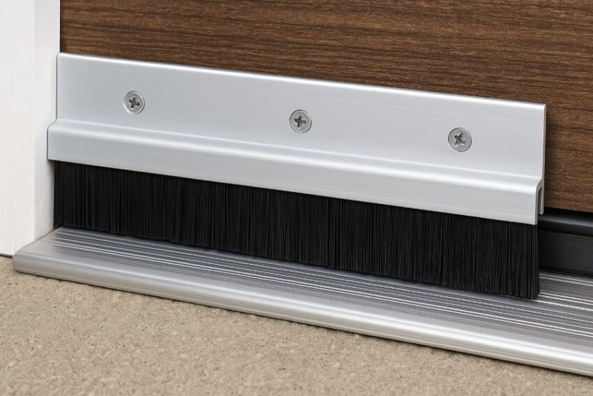 Installed aluminum brush door sweep sealing gap beneath exterior door threshold