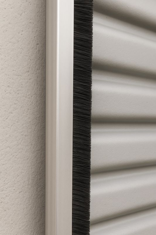 Side view of brush seal installed along corrugated roll‑up door edge, brushing against ridged surface for seamless sealing