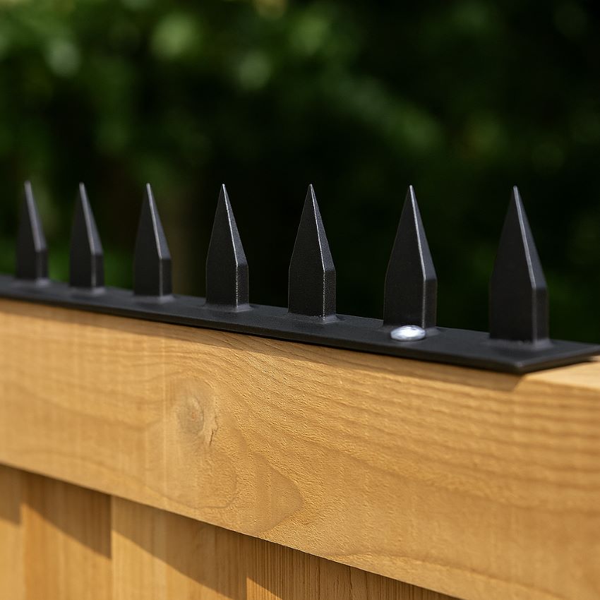 Black metal anti‑climb spikes securely installed atop a wooden fence, clearly showing sharp pointed tips.