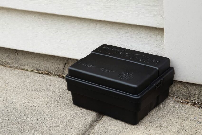 Outpost Rat Bait Station placed flush to a garage wall for safe, effective rodent control