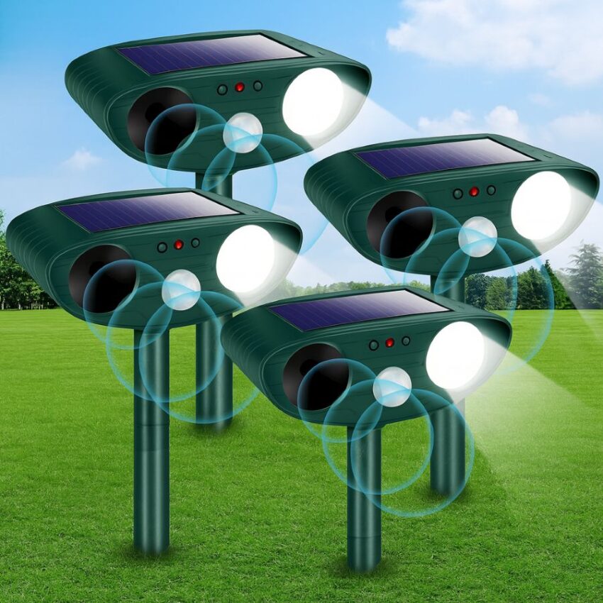 Solar ultrasonic animal repellent 4-pack staked along a garden bed, motion-triggered LEDs flashing