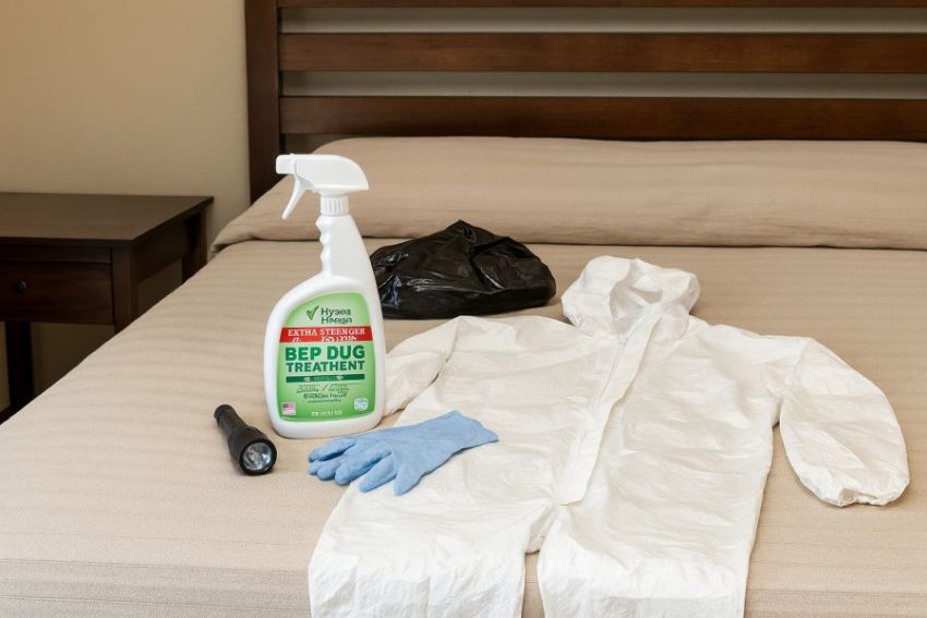 Bed bug spray 24 oz, gloves, and a disposable hooded coverall set out beside a bed for targeted treatment